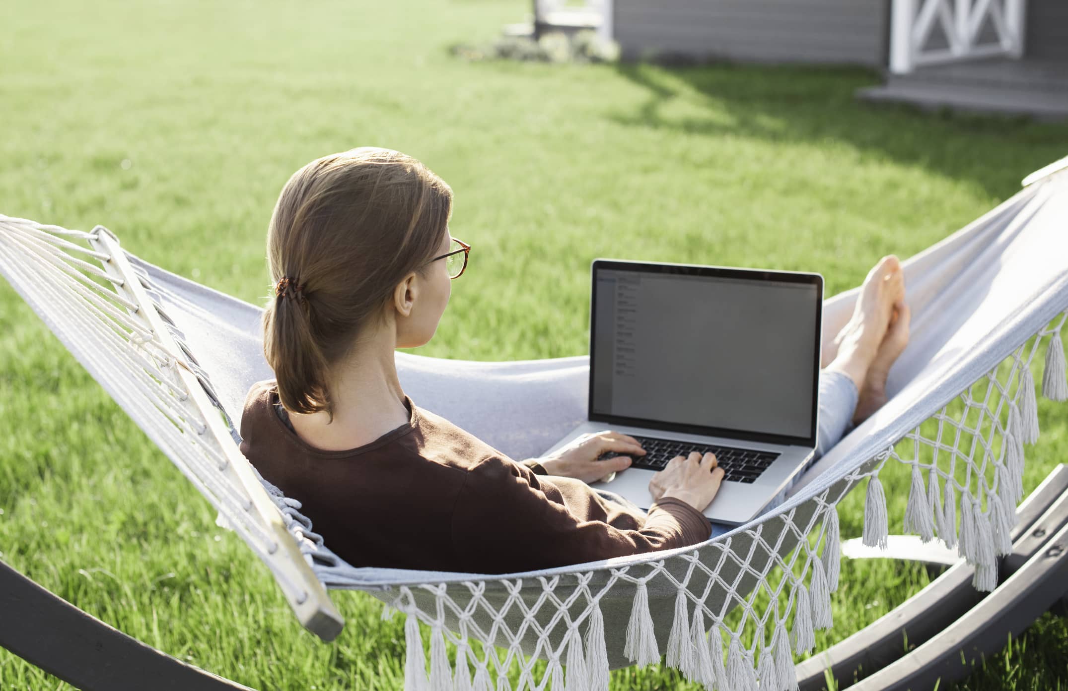 Eine Frau mit Brille sitzt in der Hängematte mit ihrem Laptop und kümmert sich um ihre Weiterentwicklung
