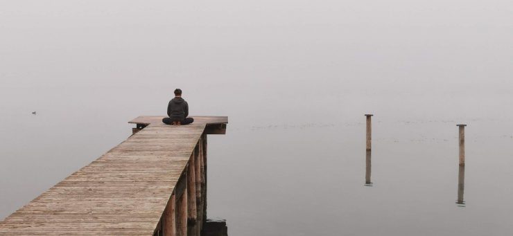 Mann meditiert am See - Coronavirus: Was Ihrem Mindset und Ihrer Geldanlage gutut