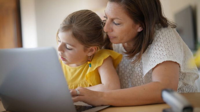 Eine Mutter sitzt mit ihrer Tochter vorm Laptop und lernt ihr Umgang mit Geld.