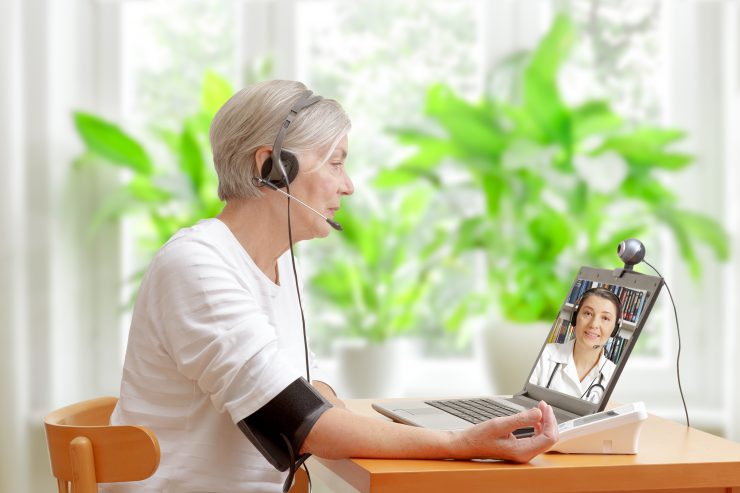 Eine ältere Dame unterhält sich online mit einer Ärztin während sie ihren Blutdruck misst - Telehealth.