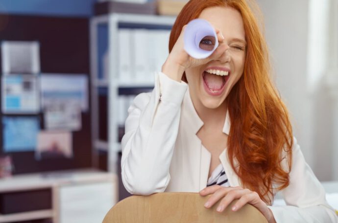 Eine Frau lugt lachend durch eine Papierrolle - so kurbelst du deine Motivation im Job wieder an