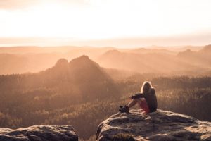Frau sitzt am Berg: Corona Spartipps für künftige Urlaube