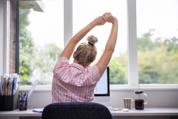Eine Frau streckt sich vor dem Laptop - Tipps für motiviertes Home-Office