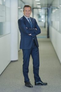 Rainer Schnabl, Vorsitzender der GF bei RCM, steht mit verschränkten Armen am Gang eines Bürogebäudes. Forum Nachhaltige Geldanlagen