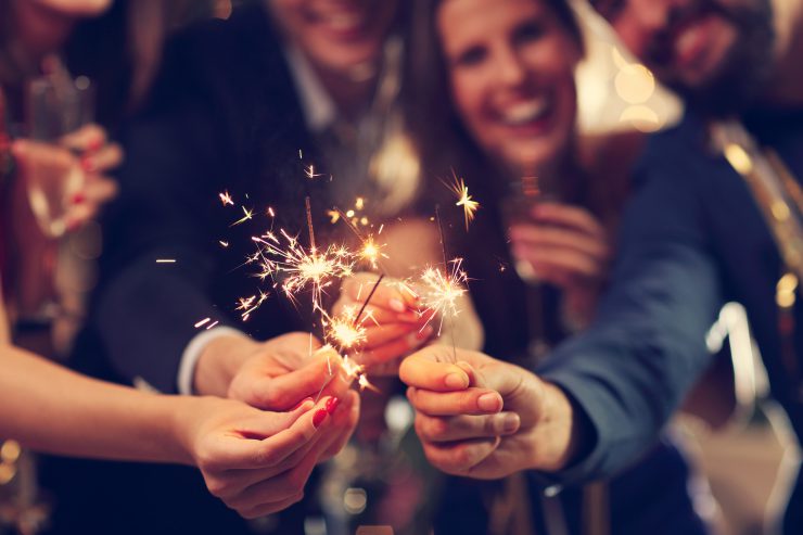 Feiernde Menschen halten Sternspritzer aneinander - ein Jahresrückblick.