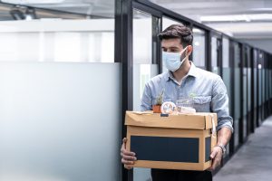 Ein Mann mit Mundschutz trägt eine Kiste mit seinen Sachen aus einem Büro.