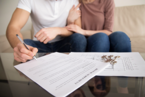 Der Partner unterschreibt den am Tisch liegenden Mietvertrag für die erste gemeinsame Wohnung.