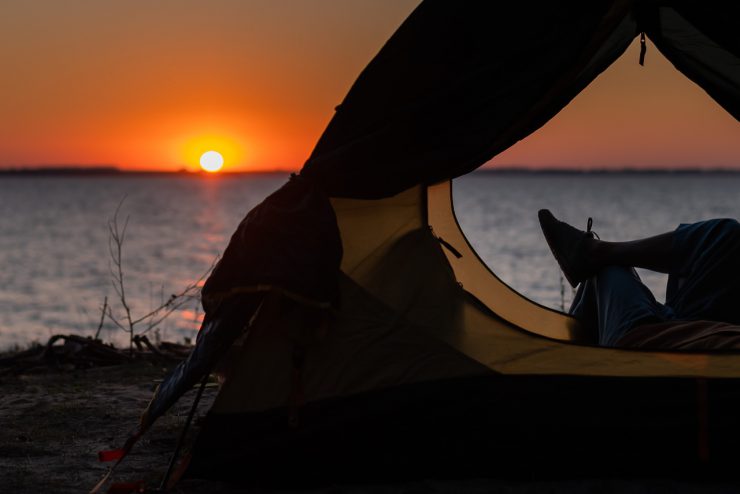 Jemand liegt im Zelt am Meer und betrachtet den Sonnenaufgang - eine Art seine finanzielle Freiheit zu genießen.