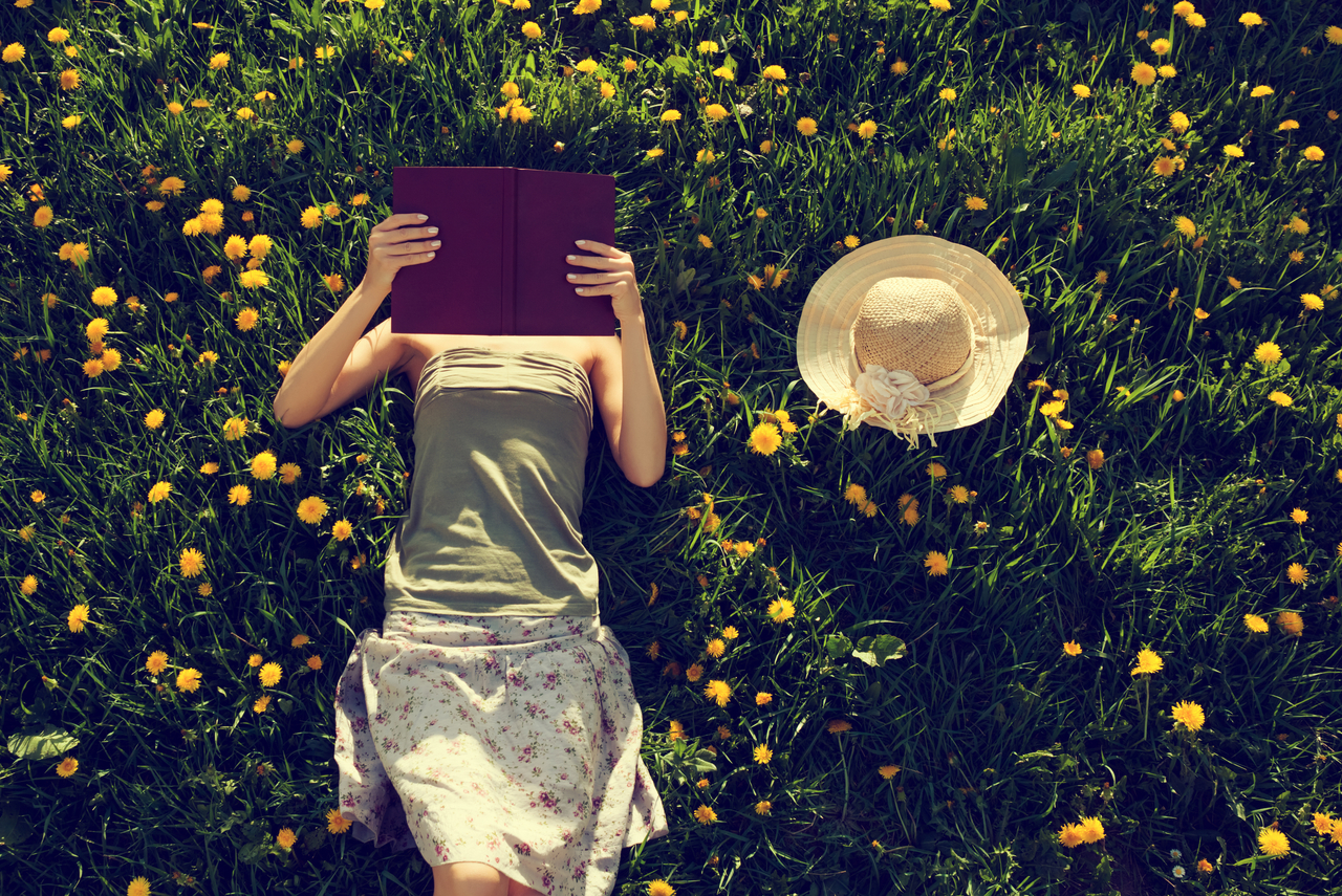 Frau liegt im Gras und liest ein Buch - 7 Bücher, die Ihr Leben nachhaltig verändern können