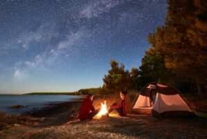 2 Menschen sitzen am Feuer beim Zelt - die Zeit im Sommer für Neues nutzen