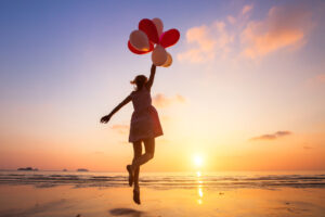 Frau tanzt mit Luftballons am Strand
