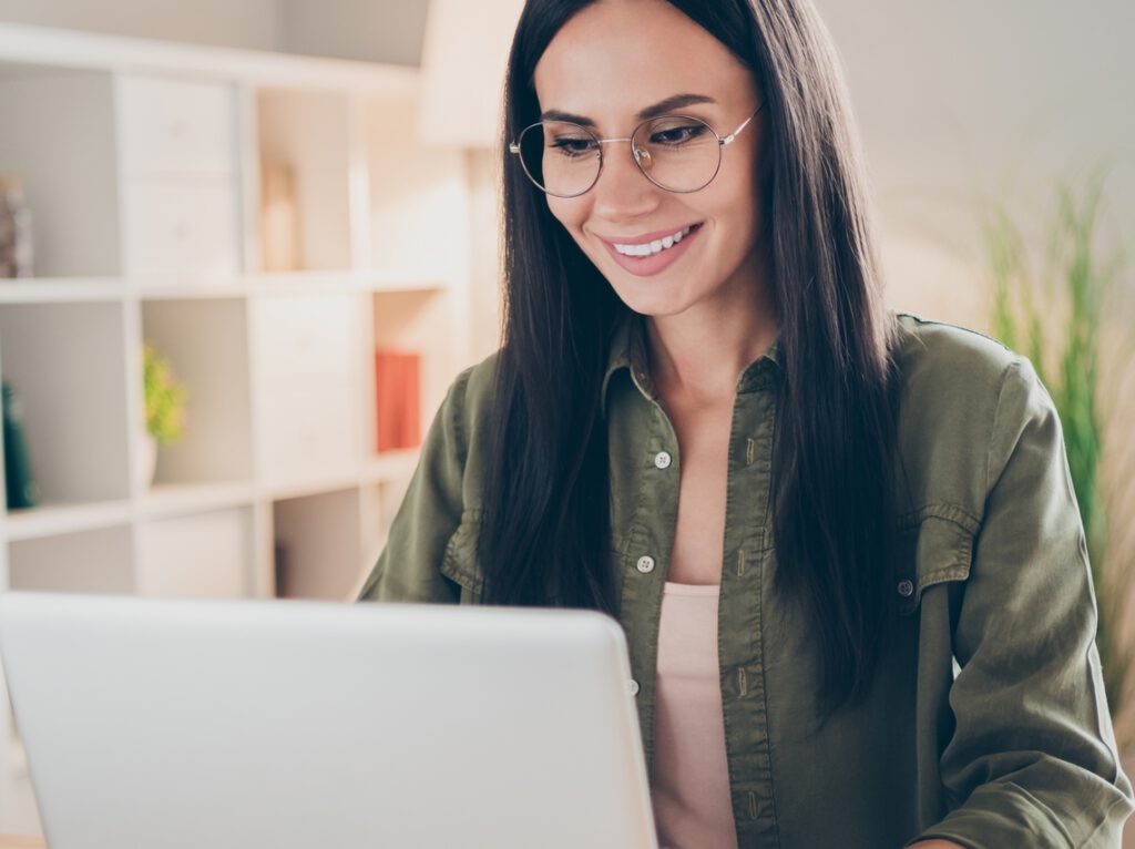 Frau mit grüner Bluse und Brille sitzt lächelnd vor PC - Nachhaltigkeit als Gamechanger für aktive Fonds