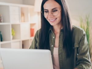 Frau mit grüner Bluse und Brille sitzt lächelnd vor PC - Nachhaltigkeit als Gamechanger und nutzt ihre Blütezeit