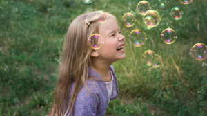 Mädchen lacht unter vielen Seifenblasen und glaubt an ihre Vision vom Leben