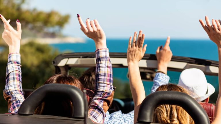 4 Menschen fahren im Cabrio mit Haenden in der Hoehe - schreib deine Summer Bucket List
