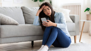 Frau sitzt am Boden mit Handy und liest schlechte Nachrichten - Tipps gegen Herbst-Blues und schlechte Nachrichten 