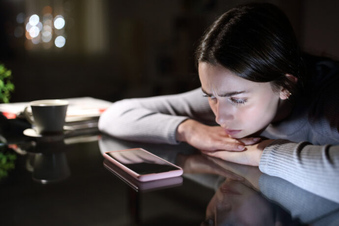 Eine Frau ängstlich nachts am Handy, unsichere Zeiten - hier sind die Tipps