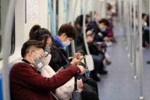 China - Menschen sitzen in der U-Bahn mit Maske und schauen Handy