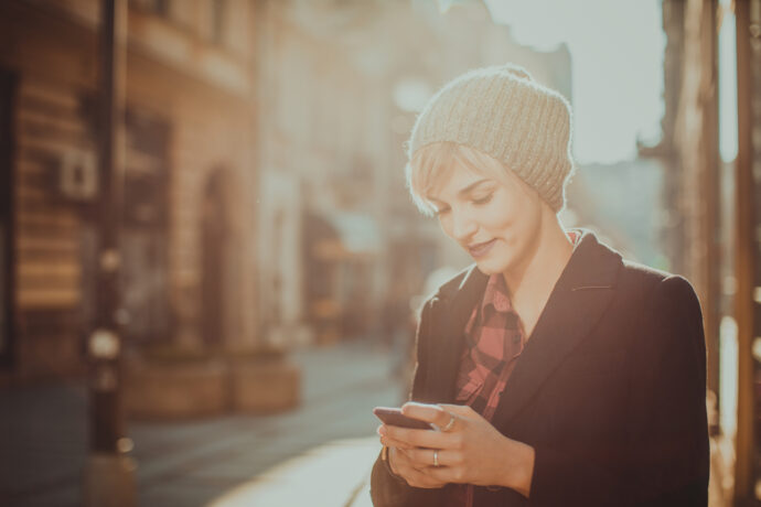 Frau mit Haube blickt lächelnd aufs Handy - Aktien steigen