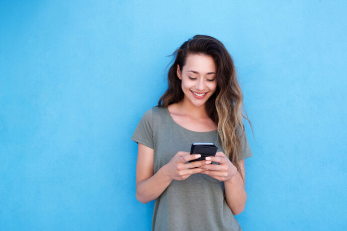 Eine Frau blickt lächelnd auf ihr Smartphone - Newsletter abonnieren
