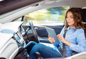 Eine Frau sitzt am Steuer eines selbstfahrenden Autos und arbeitet auf ihrem Tablet - Technologie der Zukunft.