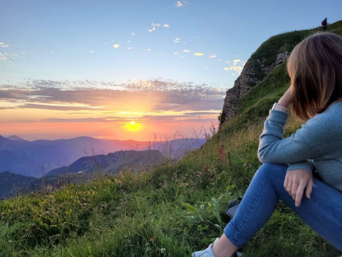 Eine junge Frau sitzt auf einem Berg und blickt in den Sonnenaufgang - Finanzplanung benötigt Weitblick.