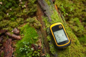 Ein GPS liegt auf einem bemoosten Holzstück - Geocaching als Freizeitbeschäftigung.