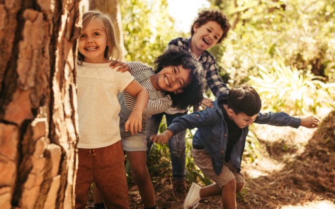 Vier Kinder spielen im Wald - eine Möglichkeit der Ferienbeschäftigung.