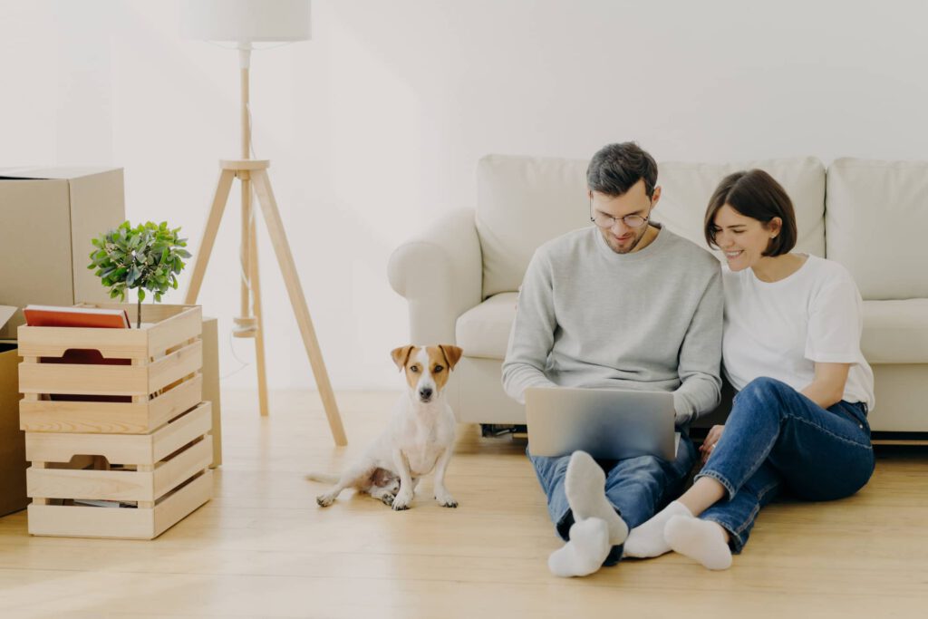 Ein Paar sitzt am Boden in der Wohnung am Laptop und investiert sanft mit Step Invest