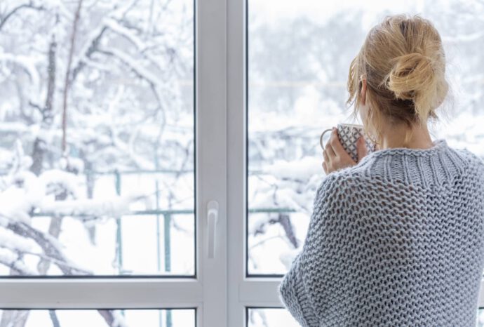 Frau blickt aus dem Fenster in den Schnee und macht Jahresrückblick