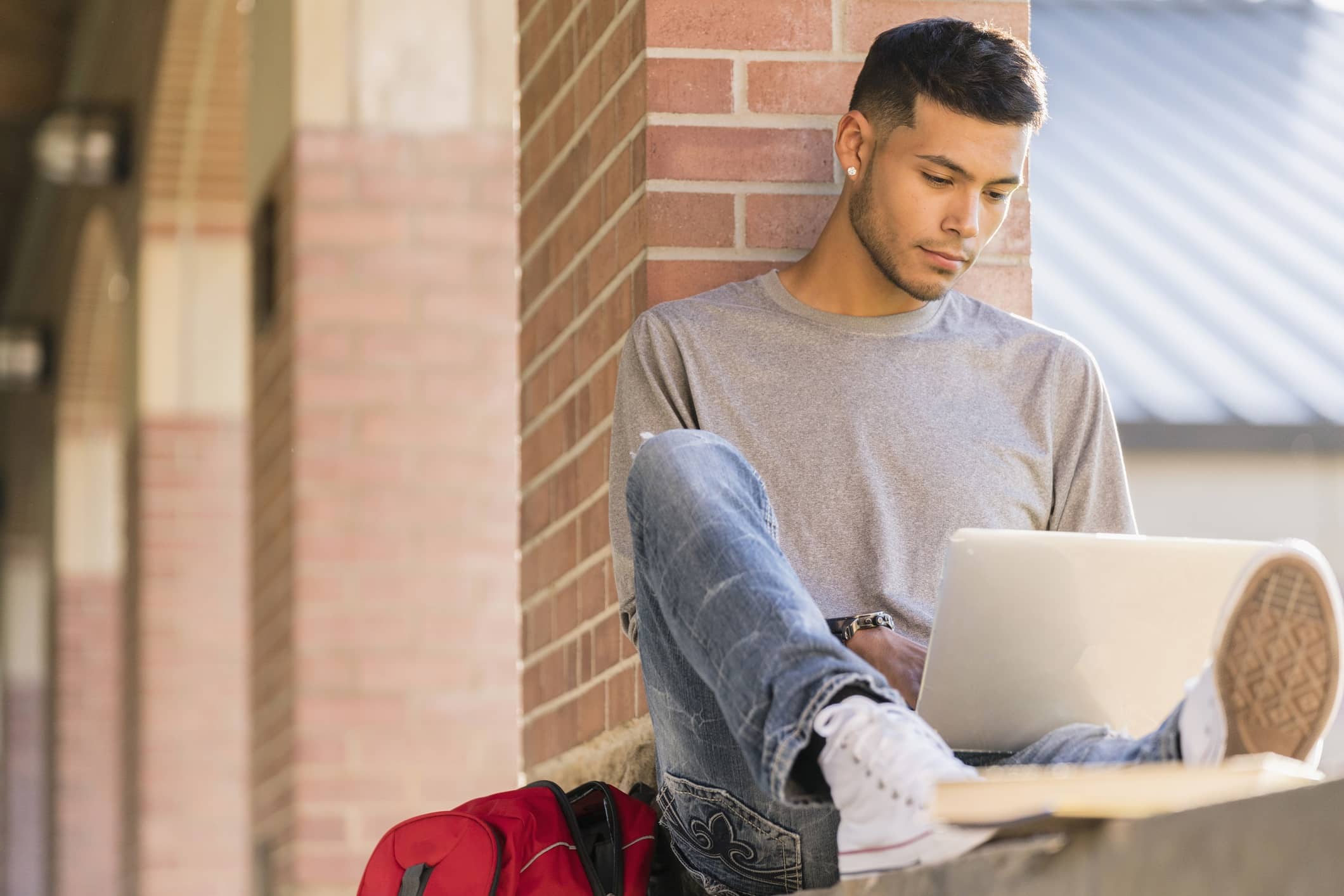 Ein junger Mann sitzt im Freien bei seinem Laptop und informiert sich über Geld anlegen.