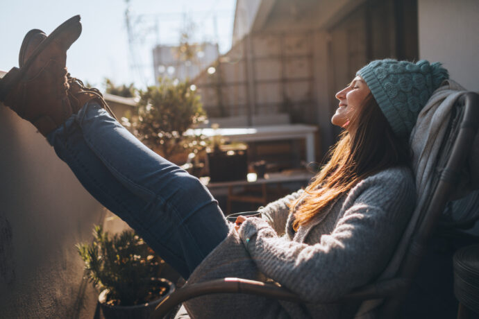 Eine Frau mit Haube entspannt sich am Balkon und lebt Minimalismus