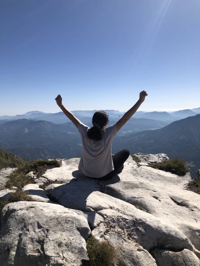 Eine Frau freut sich sitzend am Berg, sie hat mit dem Haushaltsplan ihr Ziel erreicht